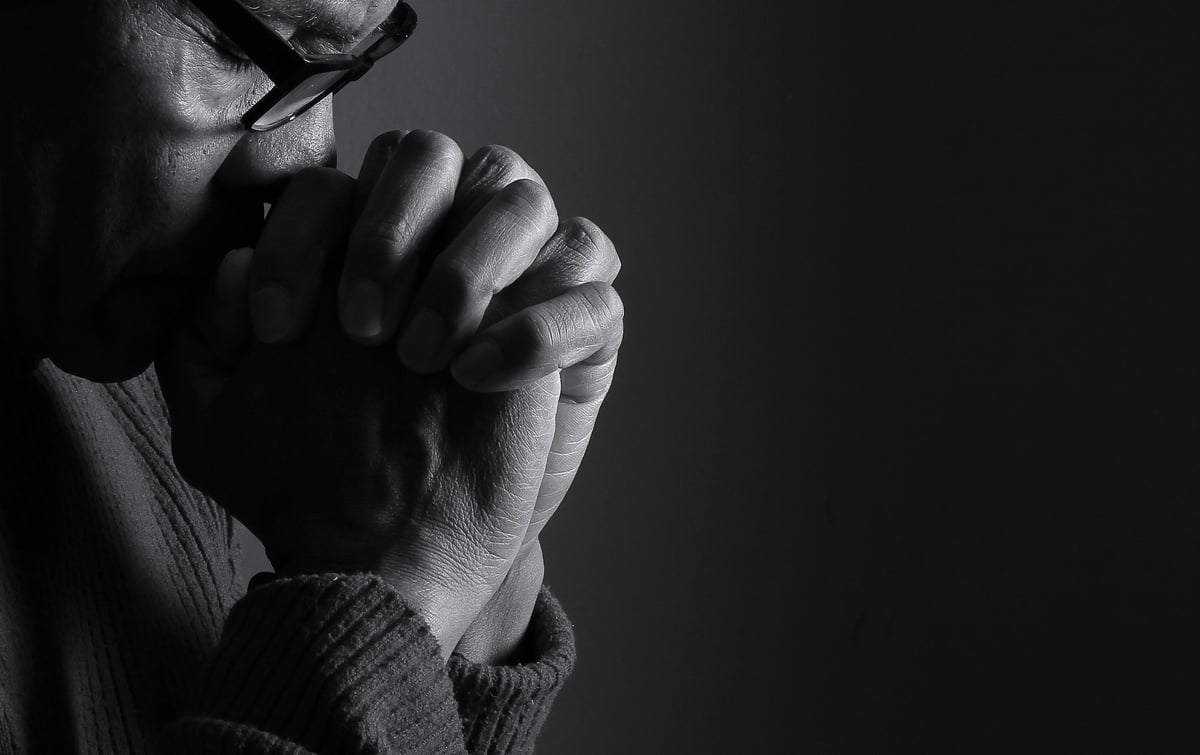 Caribbean man praying to God with hands folded after reading the bible